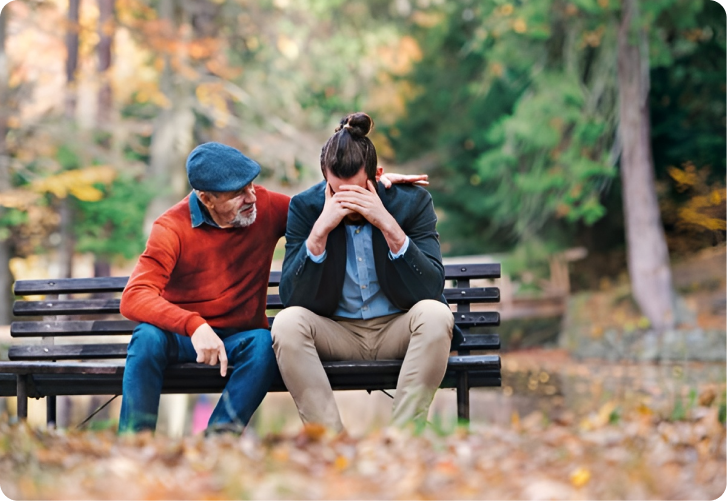 Das Bild zeigt einen älteren Herrn, der einem jüngeren Herrn, der sichtlich verzweifelt ist, aufmunternd den Arm auf die Schulter legt, sinnbildlich für psychische Erste Hilfe. 